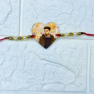 Heart-shaped personalized acrylic photo rakhi with custom printed photo, pearl and gold bead embellishments, premium red thread for Raksha Bandhan.
